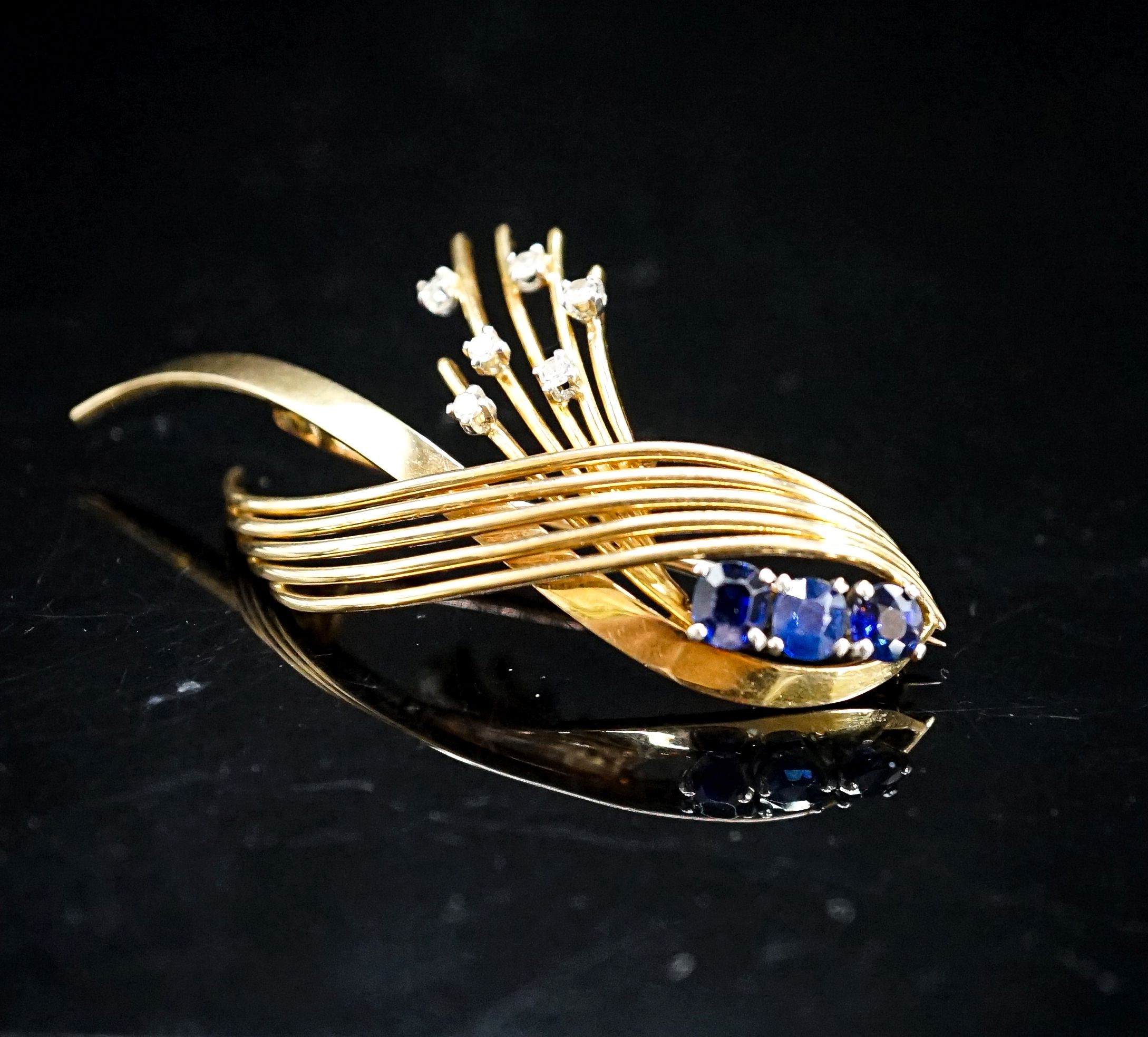 A modern yellow metal, sapphire and diamond set stylised spray brooch, 53mm, gross 9.7 grams.